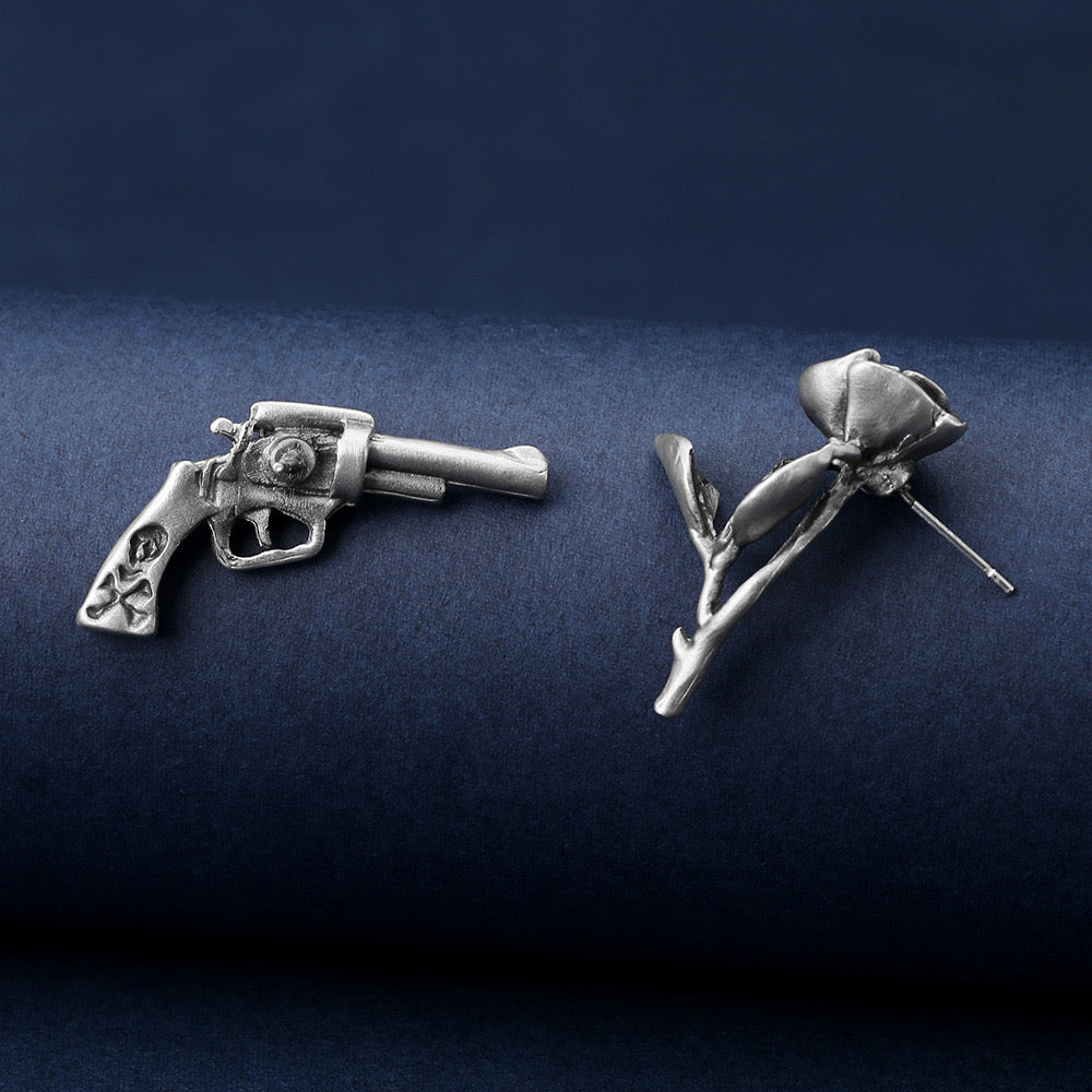 Niche storytelling rose and revolver shaped earrings